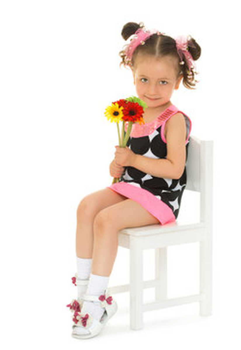 Cute little girl dressed in a short dress sits on a chair, and ...